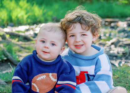 boy wearing striped dump truck sweater and baby wearing navy football sweater